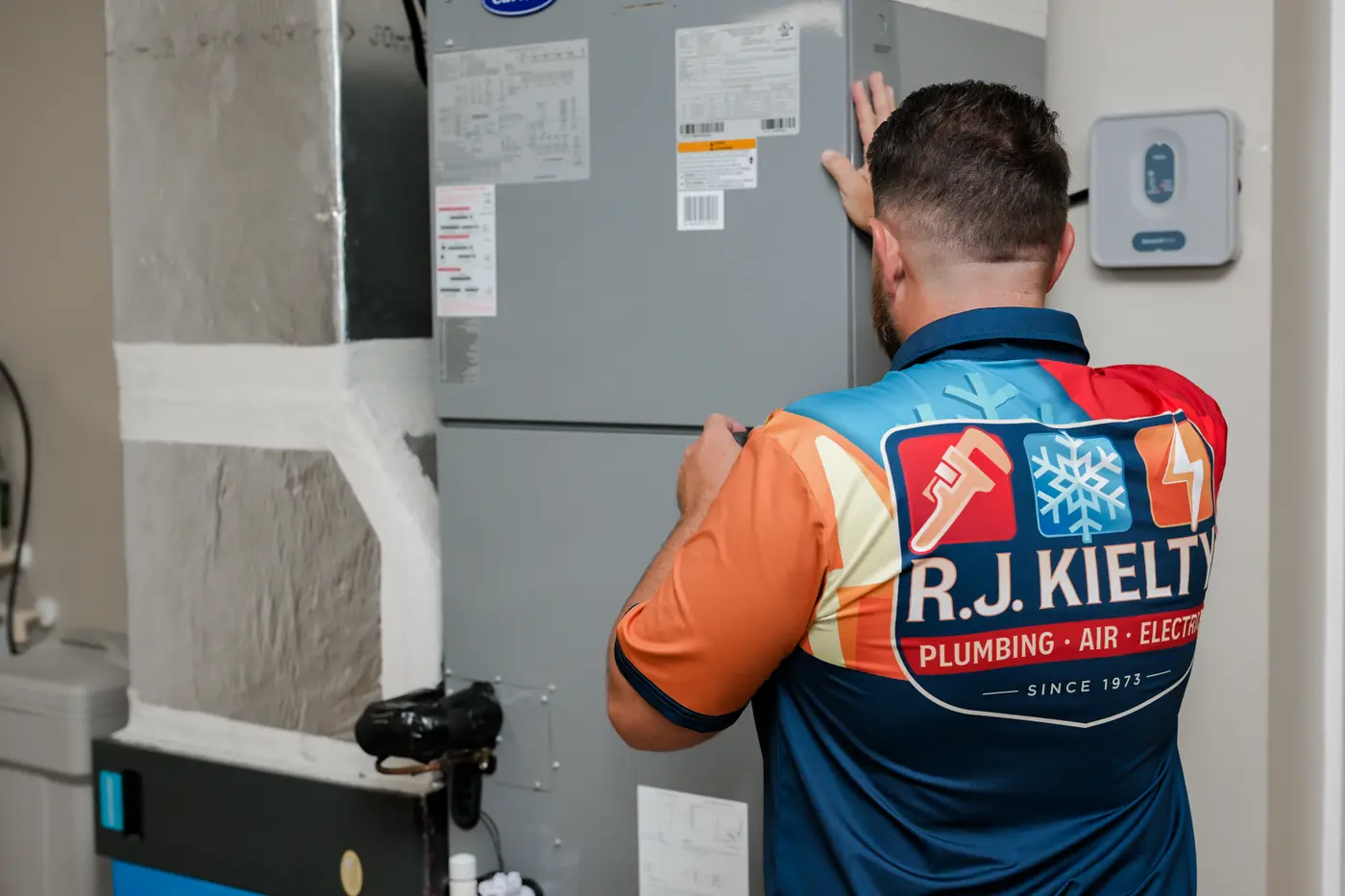 A technician inspecting an indoor air handler and its connections during a heating and cooling service